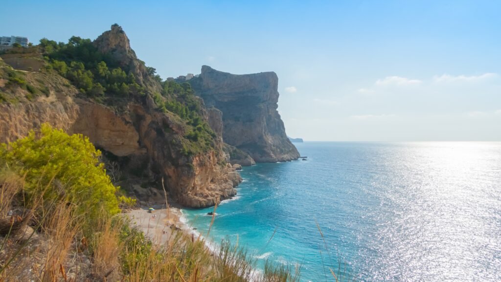 Photo of Cala del Pilar beach with turquoise waters washing against red-tinged cliffs, Menorca, Spain.
